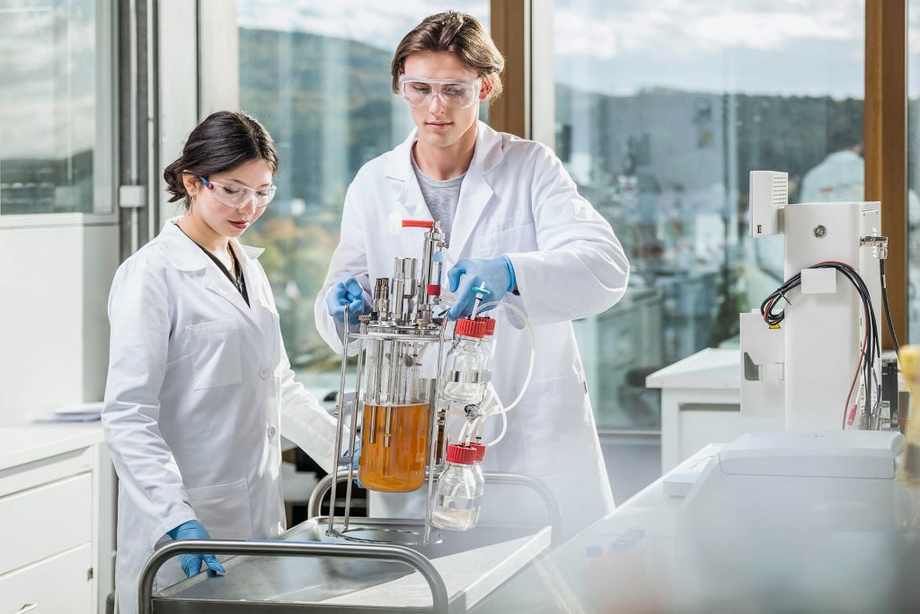 Ein Forscher und eine Forscherin stehen in weissen Kitteln in einem Labor und abrieten an einem Gerät