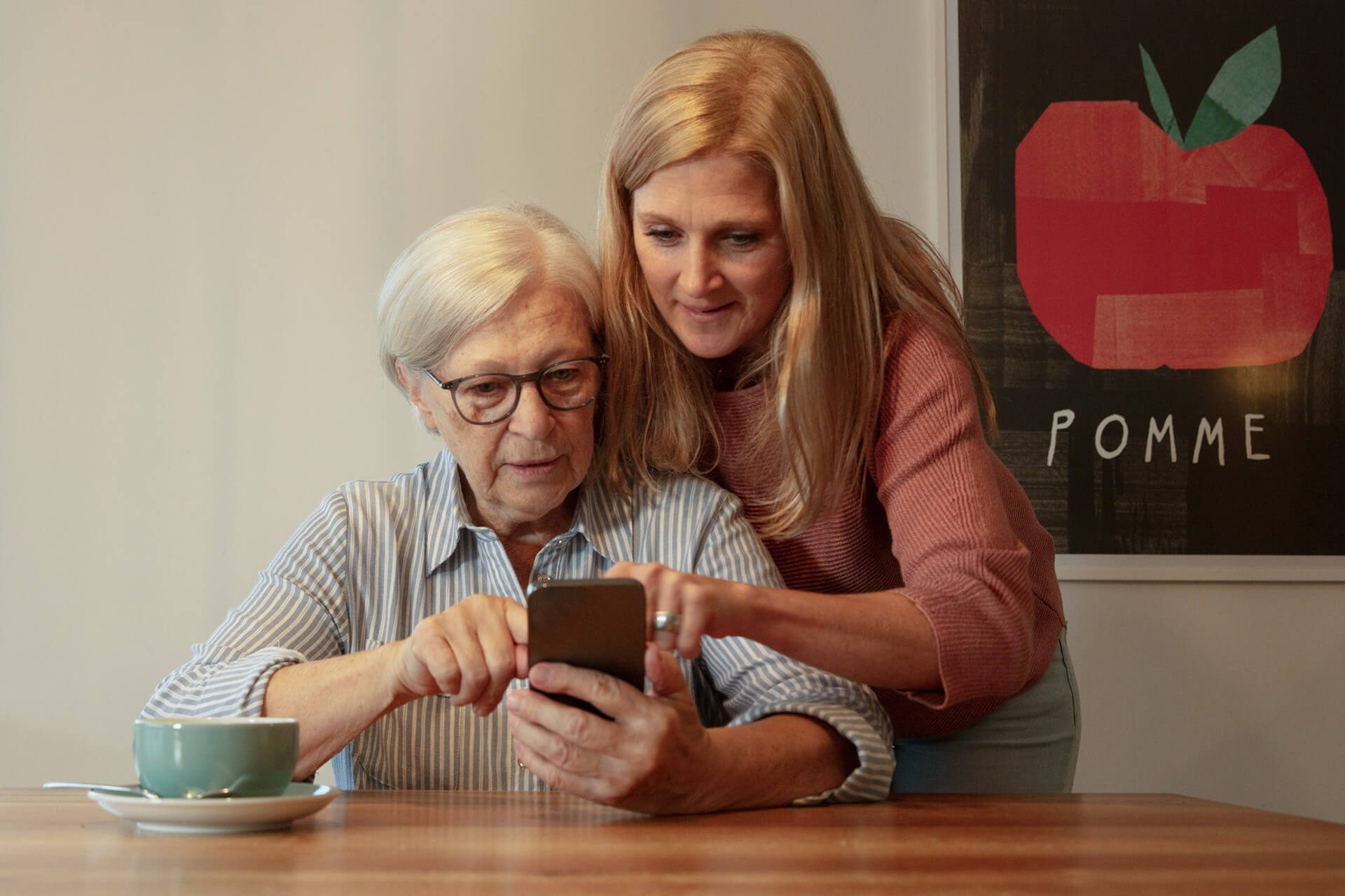 Eine jüngere Frau hilft einer älteren Frau bei der Bedienung des Smartphones.