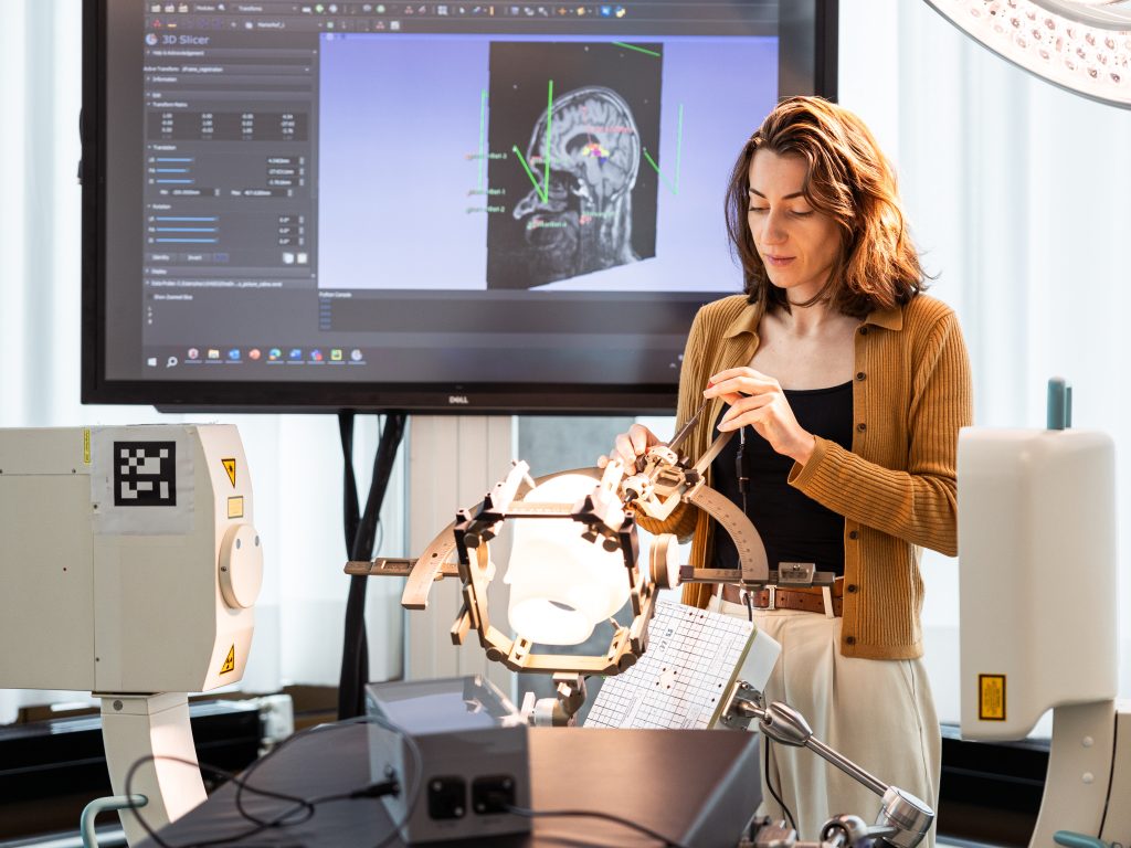 Céline Vergne arbeitet an medizinischen Geräten vor einem Monitor mit dem Bild eines Gehirn-Scans. 