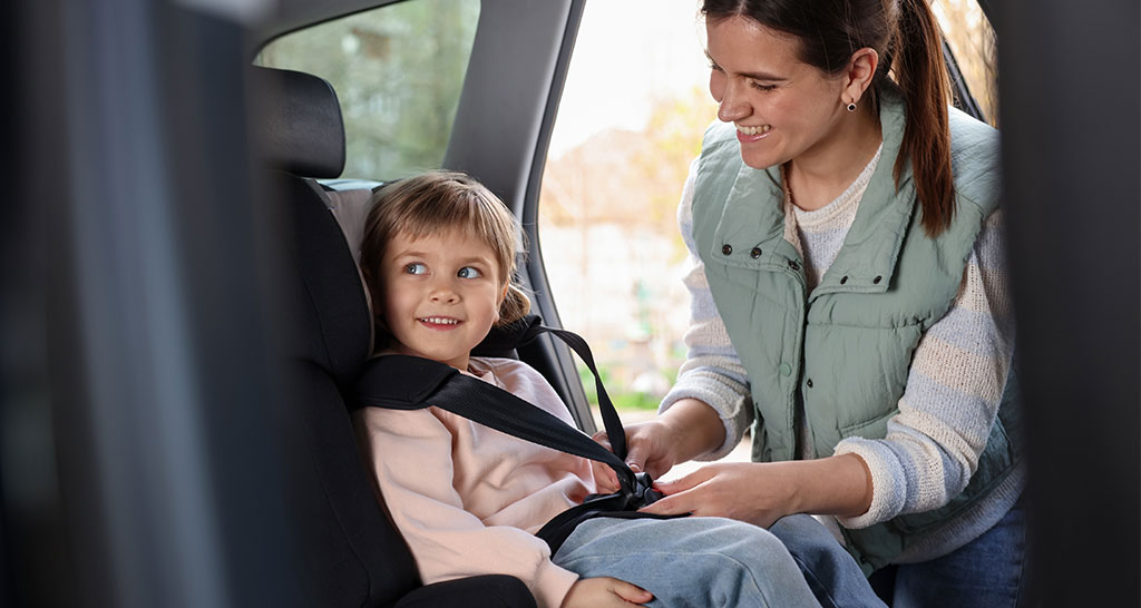 Mutter schnallt Kind im Autokindersitz an.
